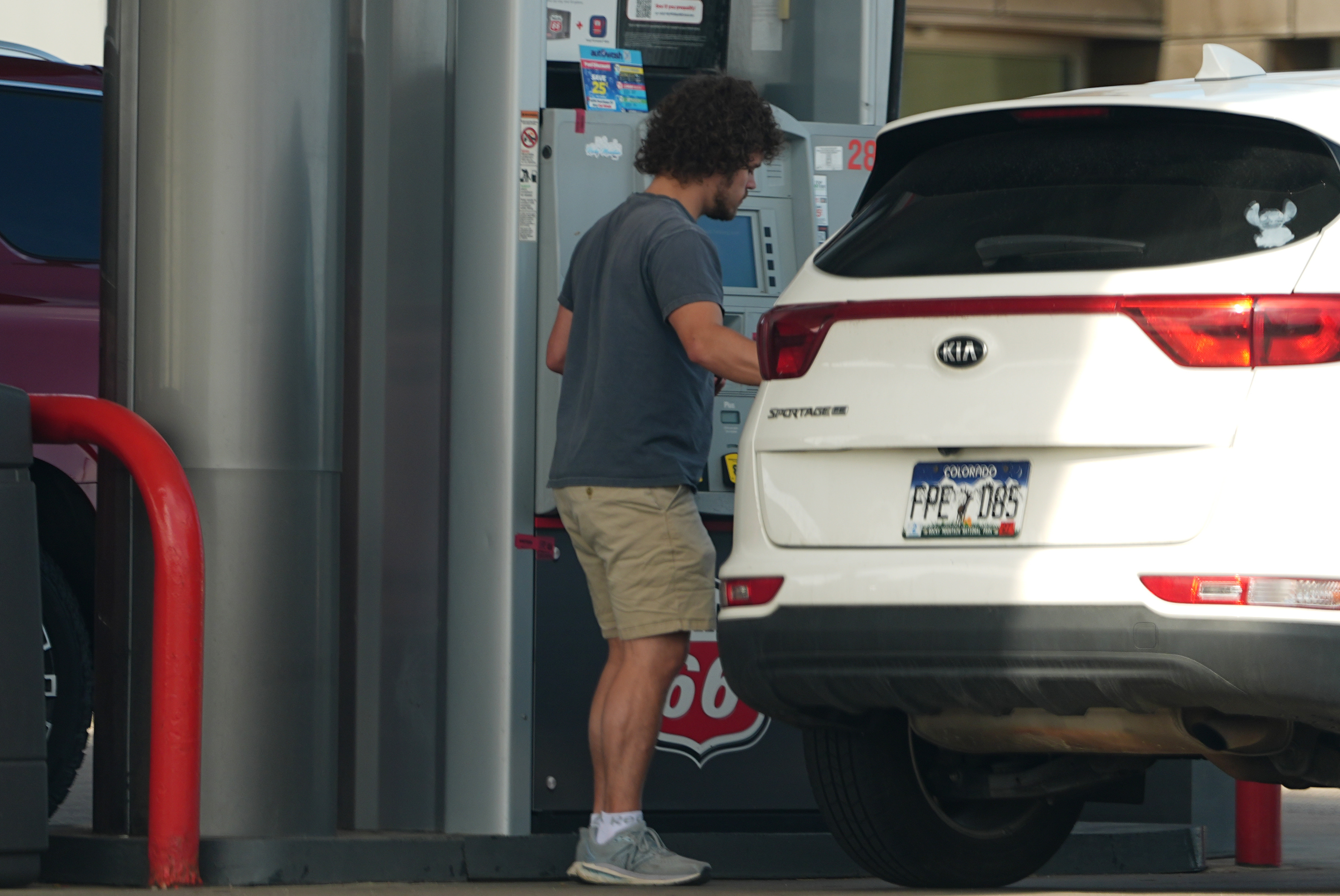 Person standing at parking garage next to white KIA Sportage SUV with license plate visible