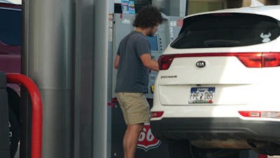 Person standing at parking garage next to white KIA Sportage SUV with license plate visible
