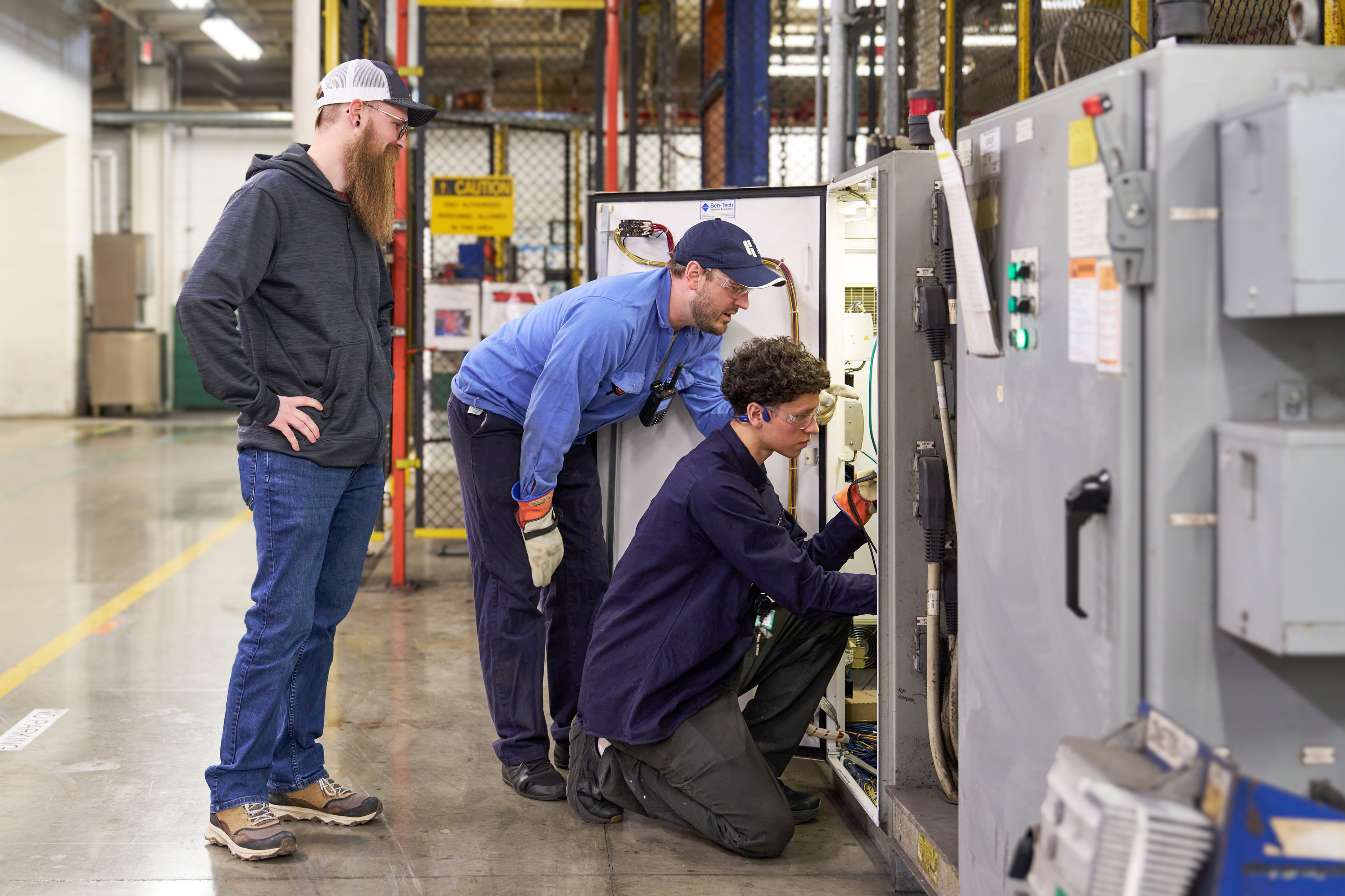 Three industrial workers inspecting electrical equipment in a manufacturing facility