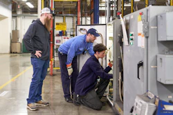 Three industrial workers inspecting electrical equipment in a manufacturing facility