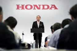 Honda executive speaking at podium during corporate press conference with attendees seated