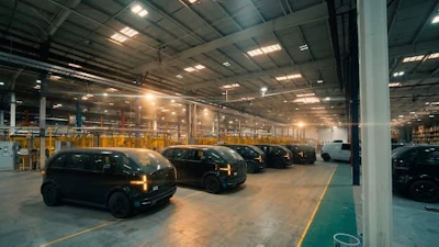 Modern automotive warehouse with rows of parked dark vehicles under industrial ceiling lights and yellow safety barriers
