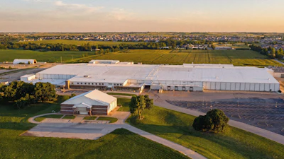 Aerial view of large industrial facility with white warehouses surrounded by green farmland and residential areas at sunset