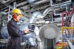 Industrial technician monitoring HVAC system with laptop in factory facility with large turbine equipment