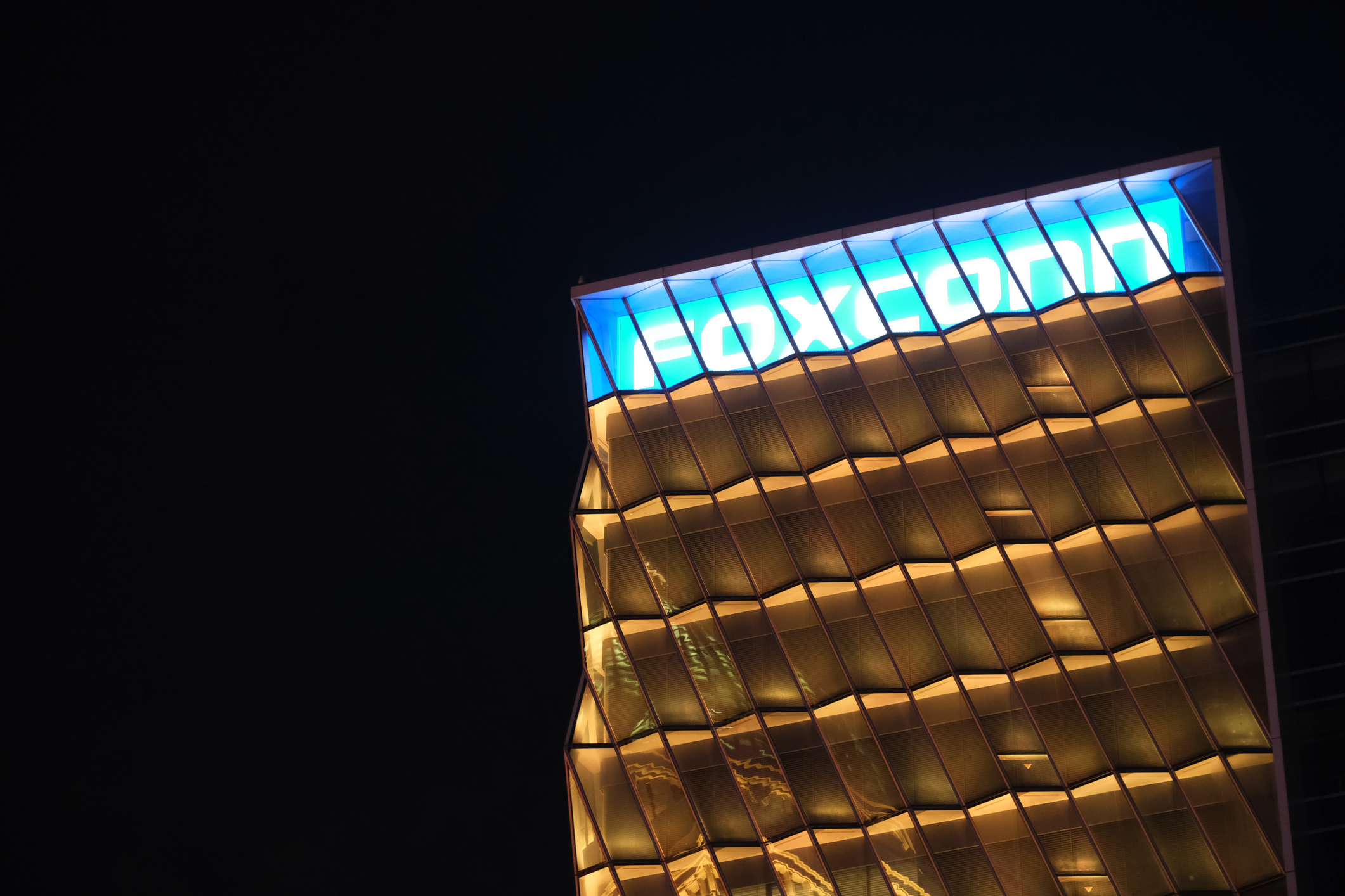Modern building facade illuminated at night with blue skylight panels and geometric gold-toned framework