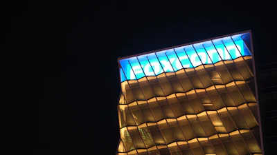 Modern building facade illuminated at night with blue skylight panels and geometric gold-toned framework
