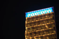 Modern building facade illuminated at night with blue skylight panels and geometric gold-toned framework