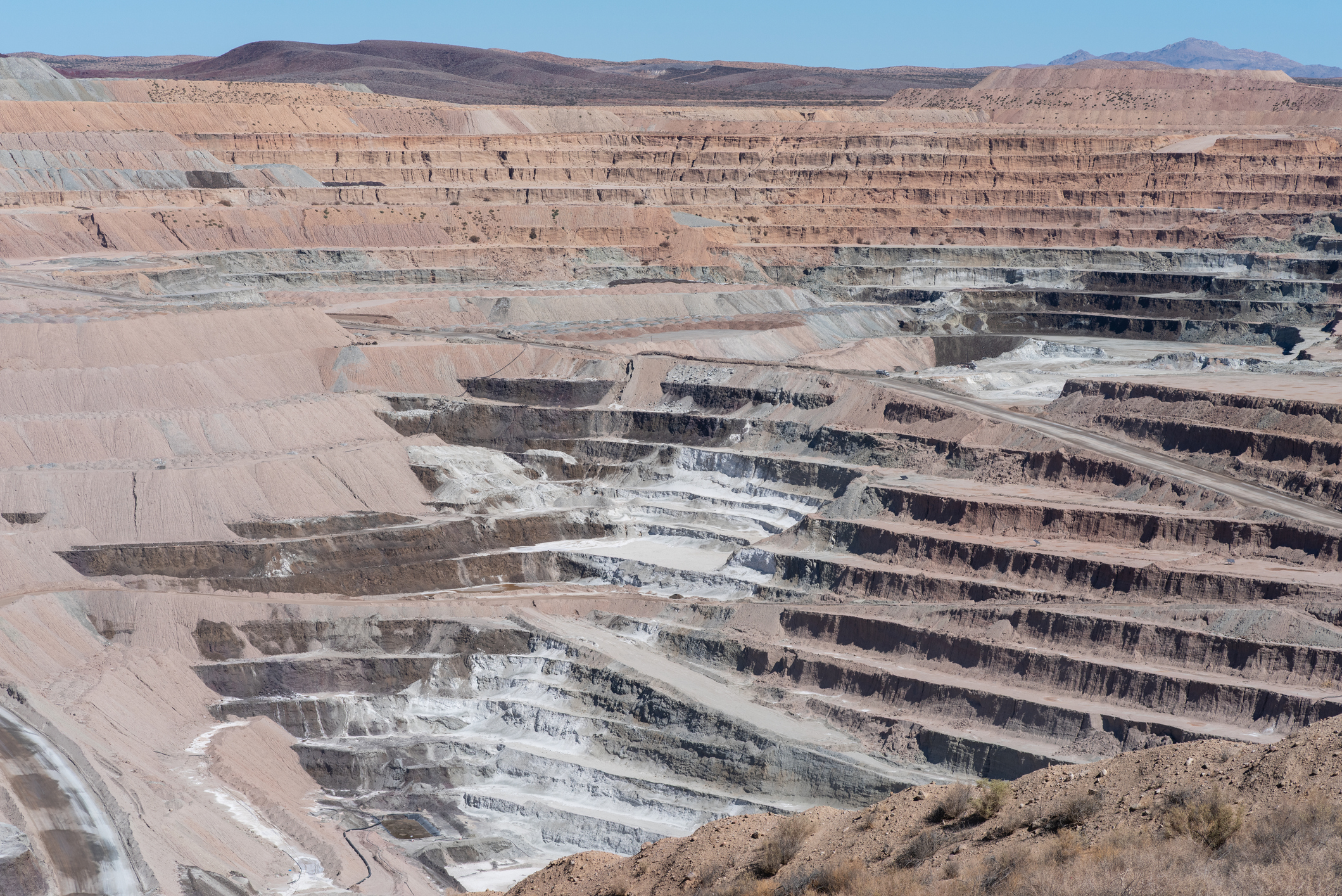 Large open-pit copper mine with terraced excavation levels and mineral deposits visible across arid desert landscape