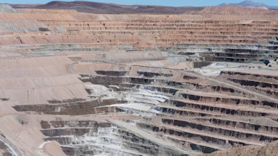 Large open-pit copper mine with terraced excavation levels and mineral deposits visible across arid desert landscape