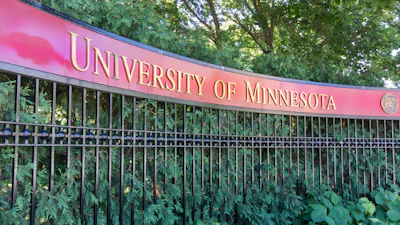 University of Minnesota pink banner sign mounted on decorative fence with green foliage backdrop