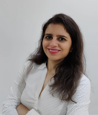 Professional headshot of a woman with long dark hair wearing a white blouse, smiling against a neutral background