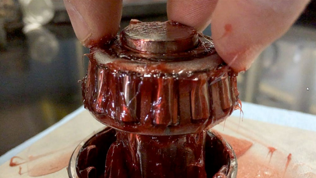 Hands holding a wet bottle cap with liquid dripping, showing product detail