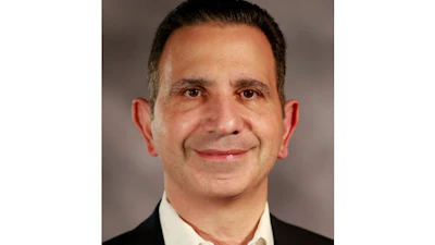Professional headshot of a middle-aged man in business attire with dark hair and a friendly smile