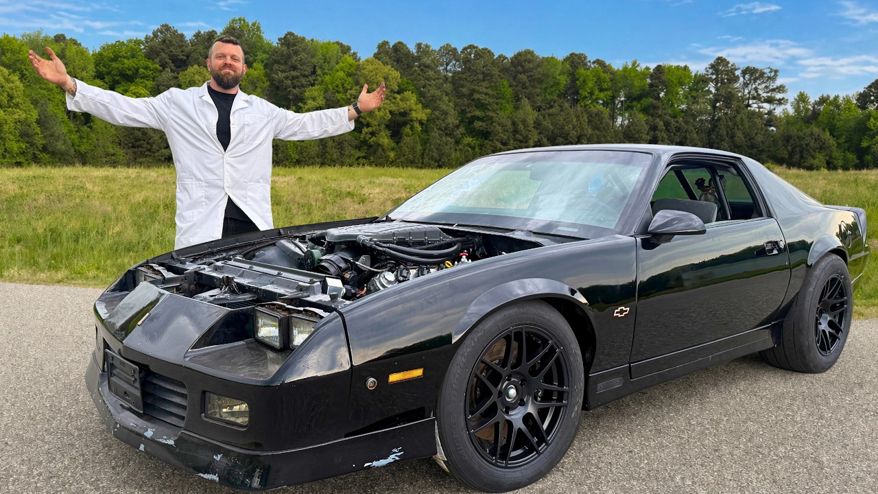 Man in white lab coat posing beside black Pontiac Firebird with open hood displaying engine