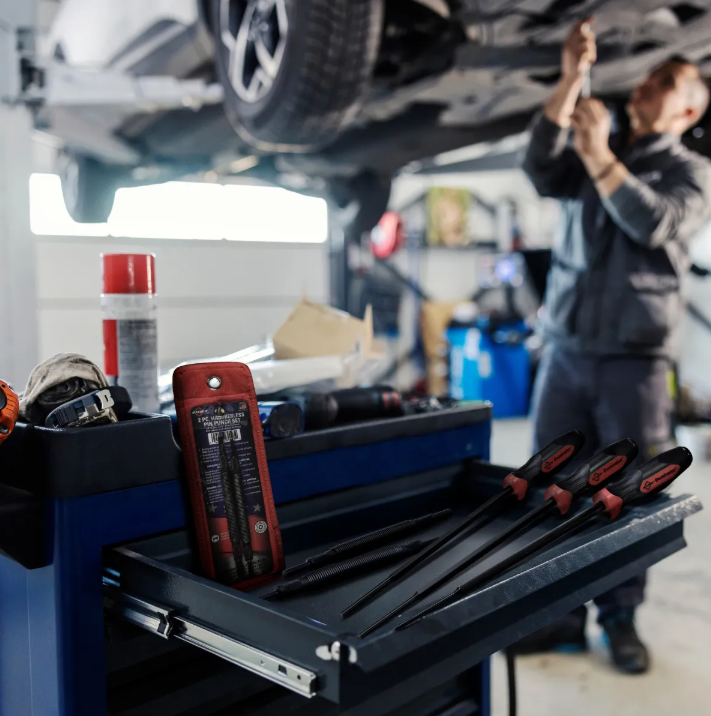 Mechanic's toolbox with multimeter and hand tools in automotive repair shop with lifted vehicle
