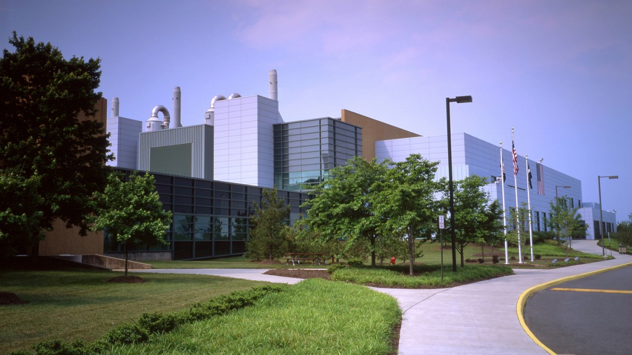 Modern architectural complex with multi-story buildings, green landscaping, and flagpoles along a curved pathway