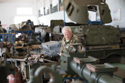 Elderly man in camouflage uniform inspecting military equipment in industrial workshop