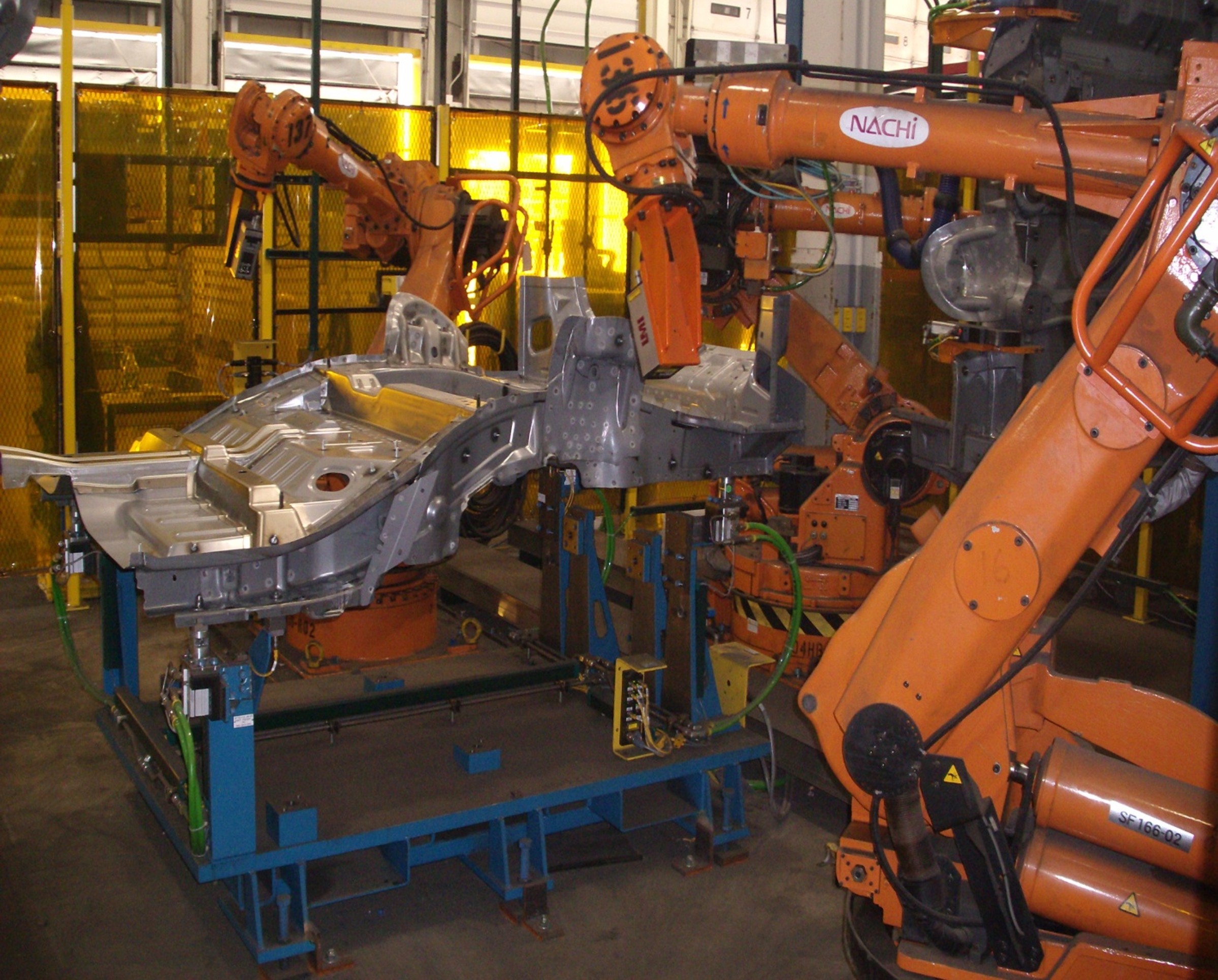 Industrial robotic welding arms with NACHI equipment at manufacturing facility workstation