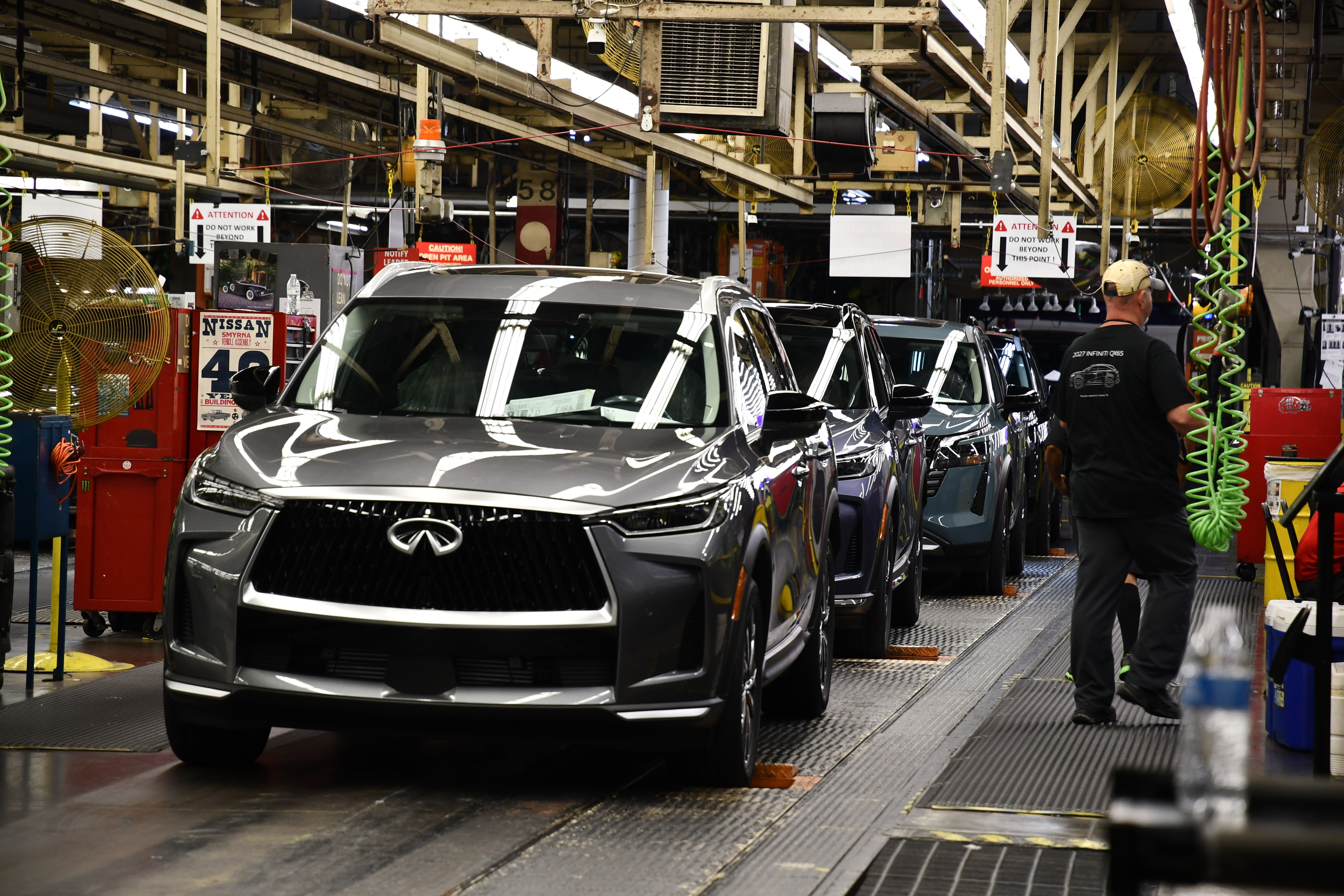 Infiniti luxury vehicles on assembly line in manufacturing plant with workers and industrial equipment