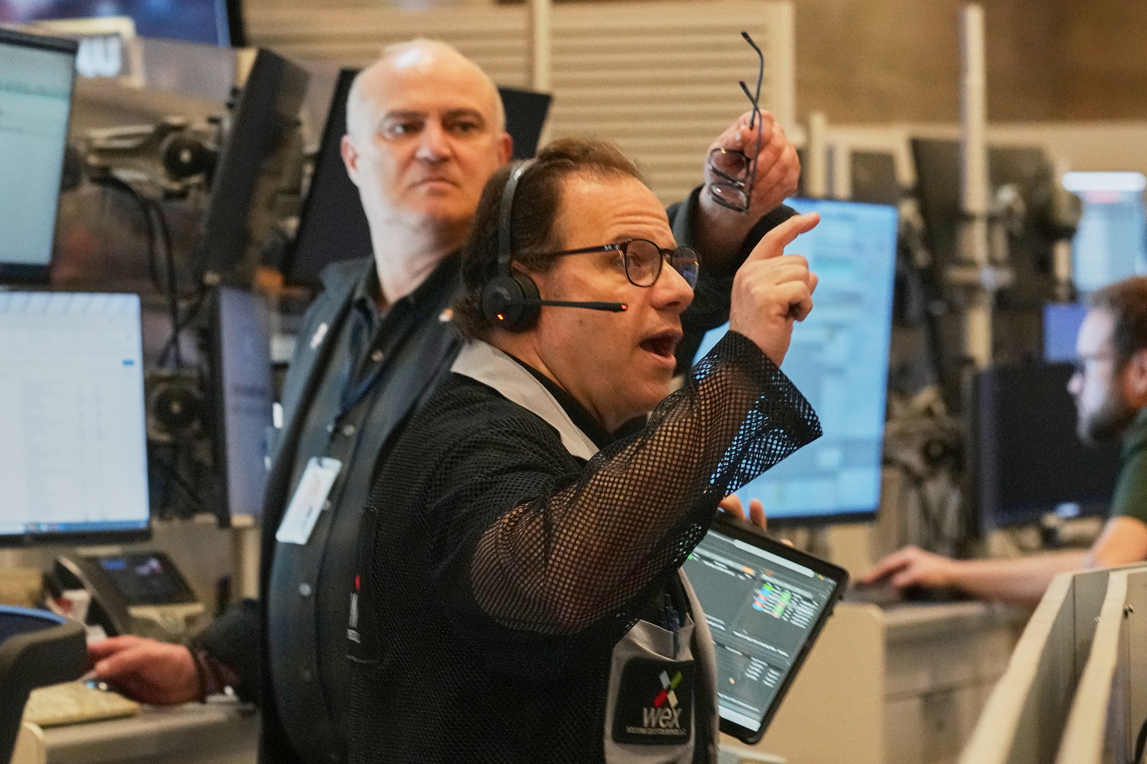 Professional in headset gesturing during broadcast studio production with colleague observing