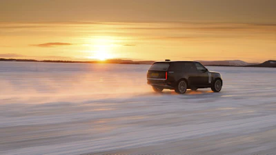 Dark luxury SUV parked on frozen lake at golden sunset with mountains in background