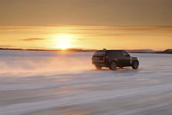 Dark luxury SUV parked on frozen lake at golden sunset with mountains in background