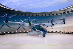 Futuristic electric aircraft displayed in museum exhibition with blue and white livery against curved wall mural