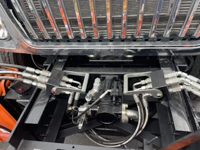 Overhead view of an orange vehicle engine bay showing mechanical components, hoses, and connectors