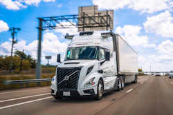 White Volvo autonomous semi-truck driving on highway with clear blue sky and traffic