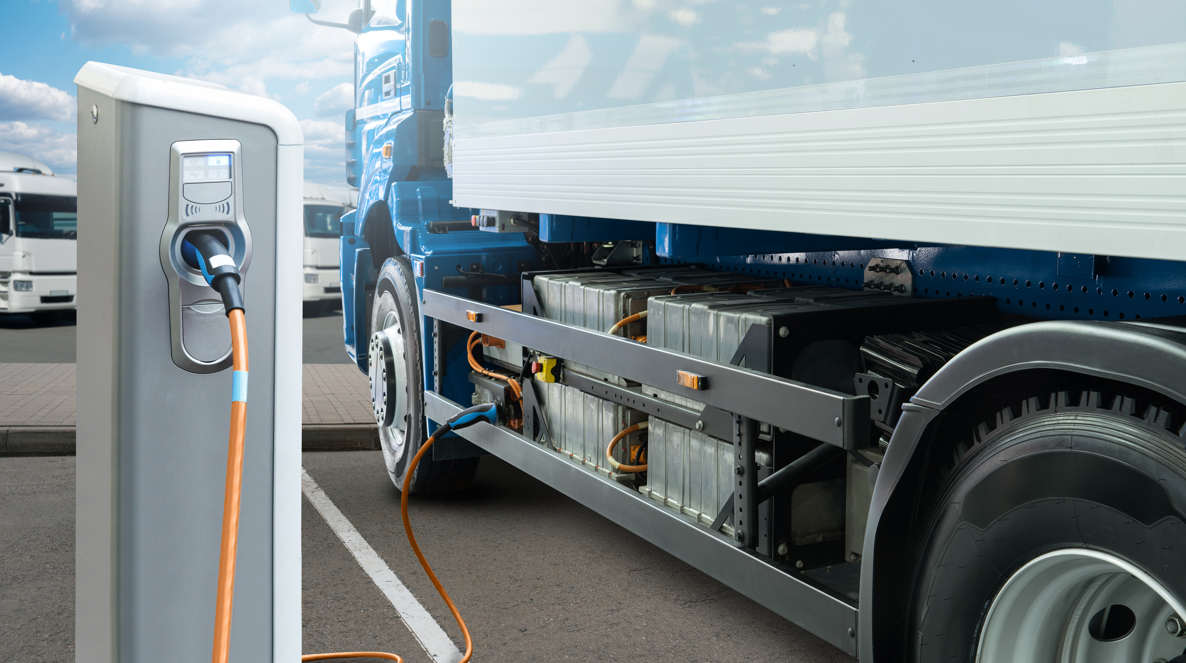 Electric vehicle charging station with orange cable connected to blue and white truck at commercial fleet facility