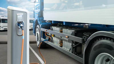 Electric vehicle charging station with orange cable connected to blue and white truck at commercial fleet facility