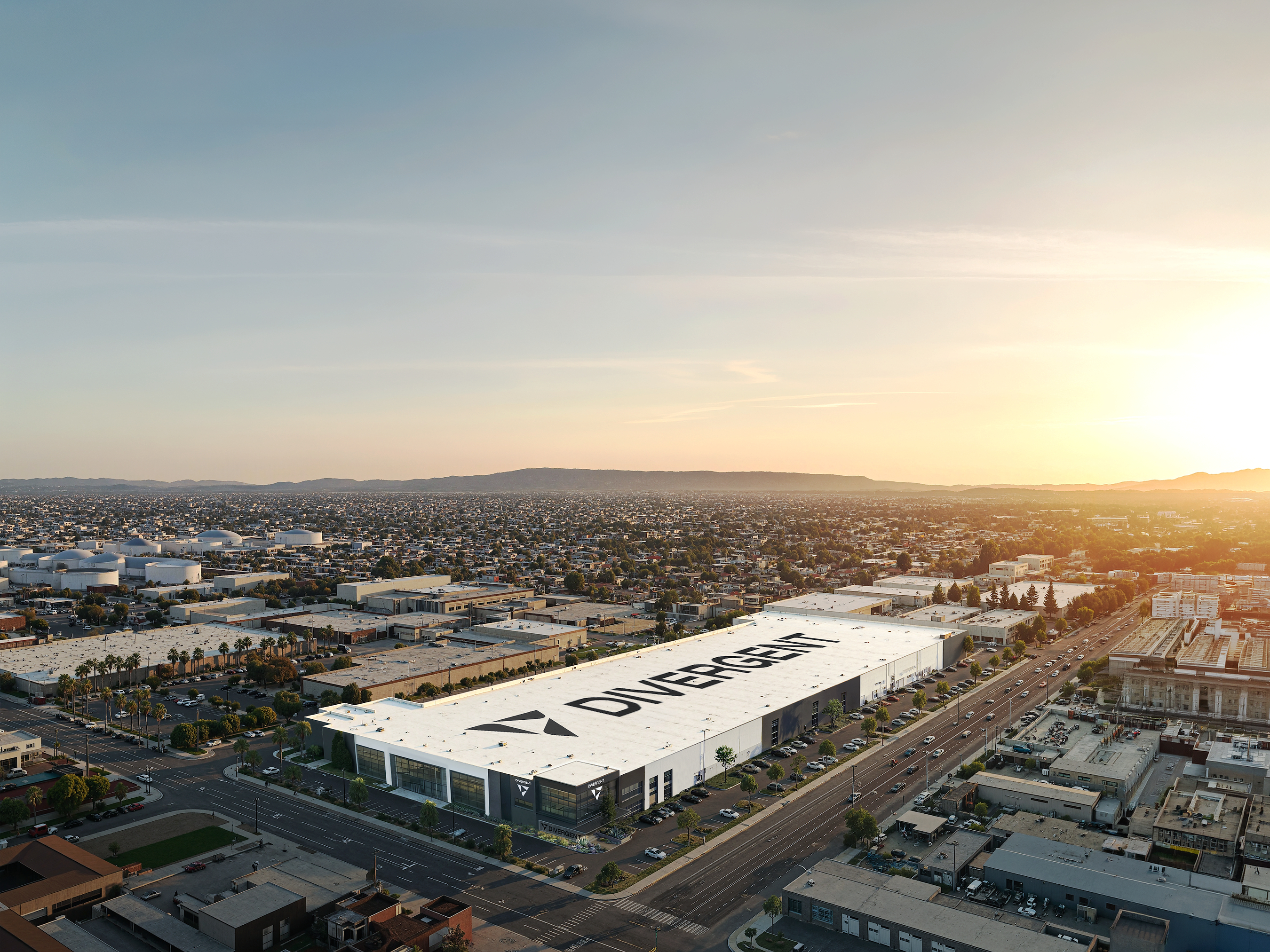 Aerial view of large white industrial facility with corporate signage in suburban landscape at sunset