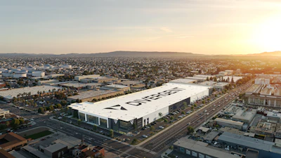 Aerial view of large white industrial facility with corporate signage in suburban landscape at sunset
