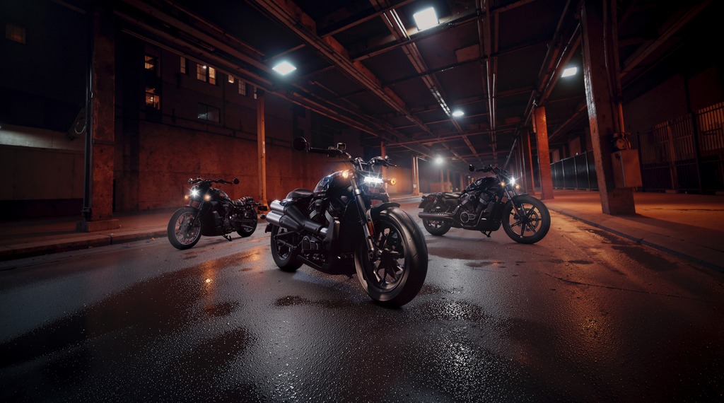 Three motorcycles parked in an industrial warehouse at night with dramatic overhead lighting and wet pavement