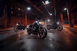 Three motorcycles parked in an industrial warehouse at night with dramatic overhead lighting and wet pavement