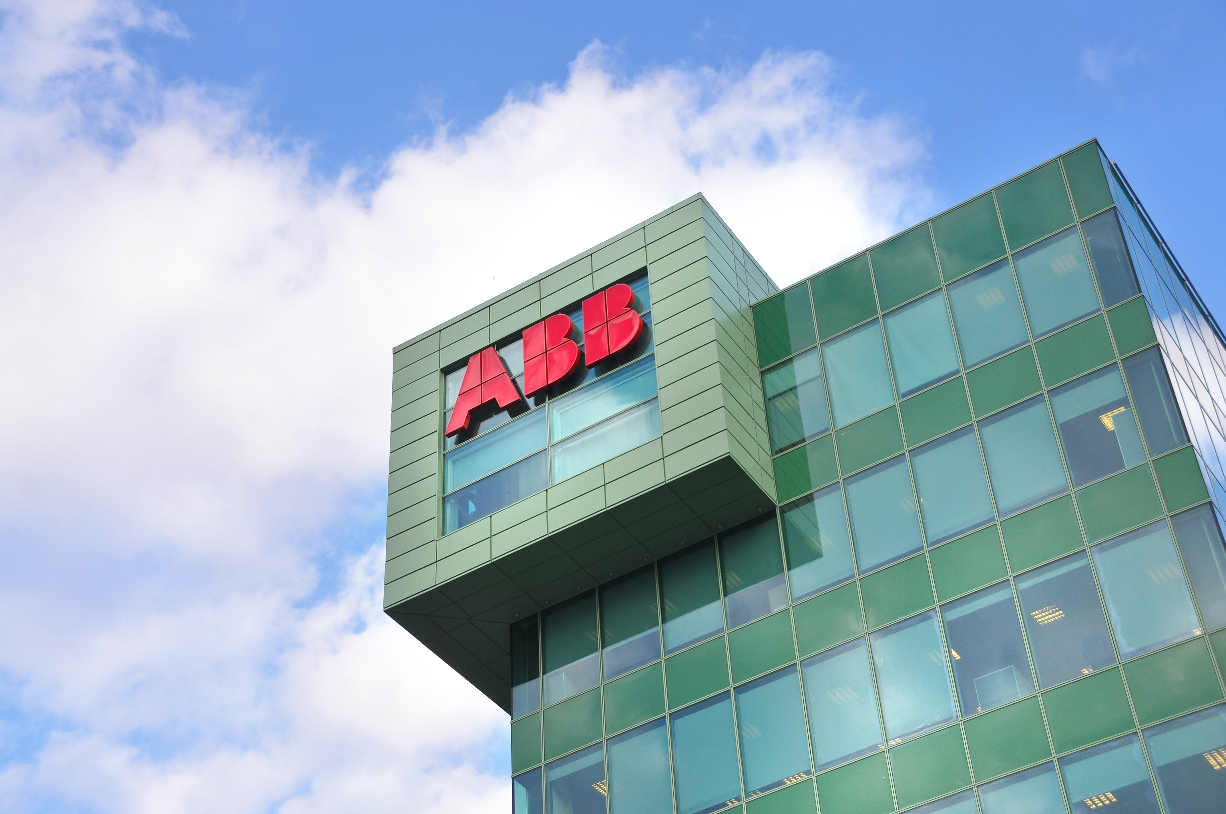 ABB red logo on modern green glass office building facade against blue sky