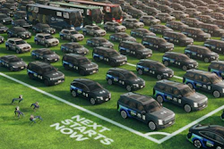 Large fleet of black police vehicles parked in organized rows on grass with white line markings and officers visible in the foreground.