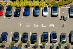 Aerial view of Tesla parking lot with multiple electric vehicles and ground branding