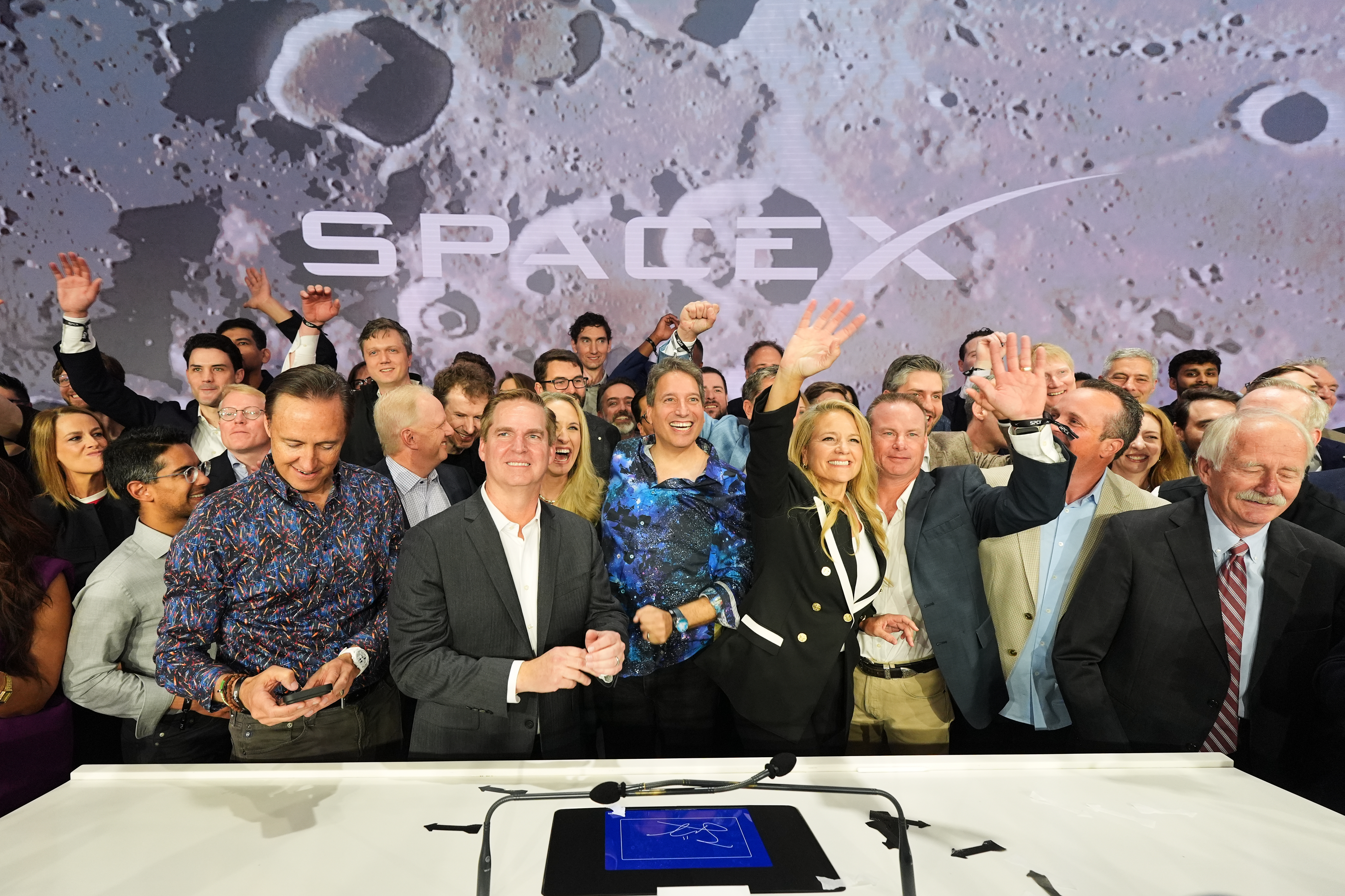 Group of SpaceX employees and officials celebrating at corporate event with lunar surface backdrop