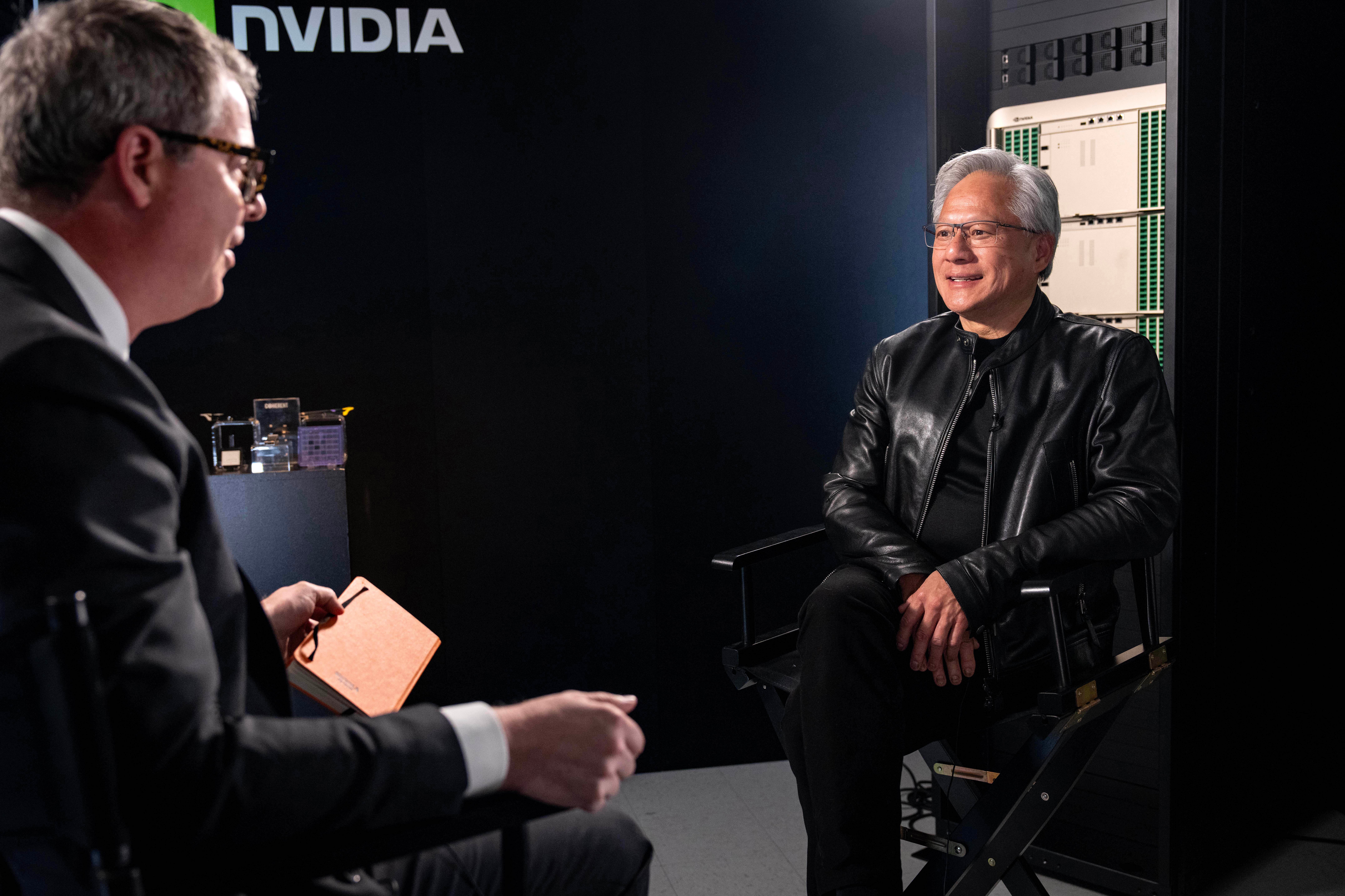 Two men in business attire having a conversation during an NVIDIA corporate event, with server equipment visible in the background.
