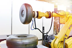 Industrial robotic arm with yellow joints and mechanical components holding a tire in a testing facility