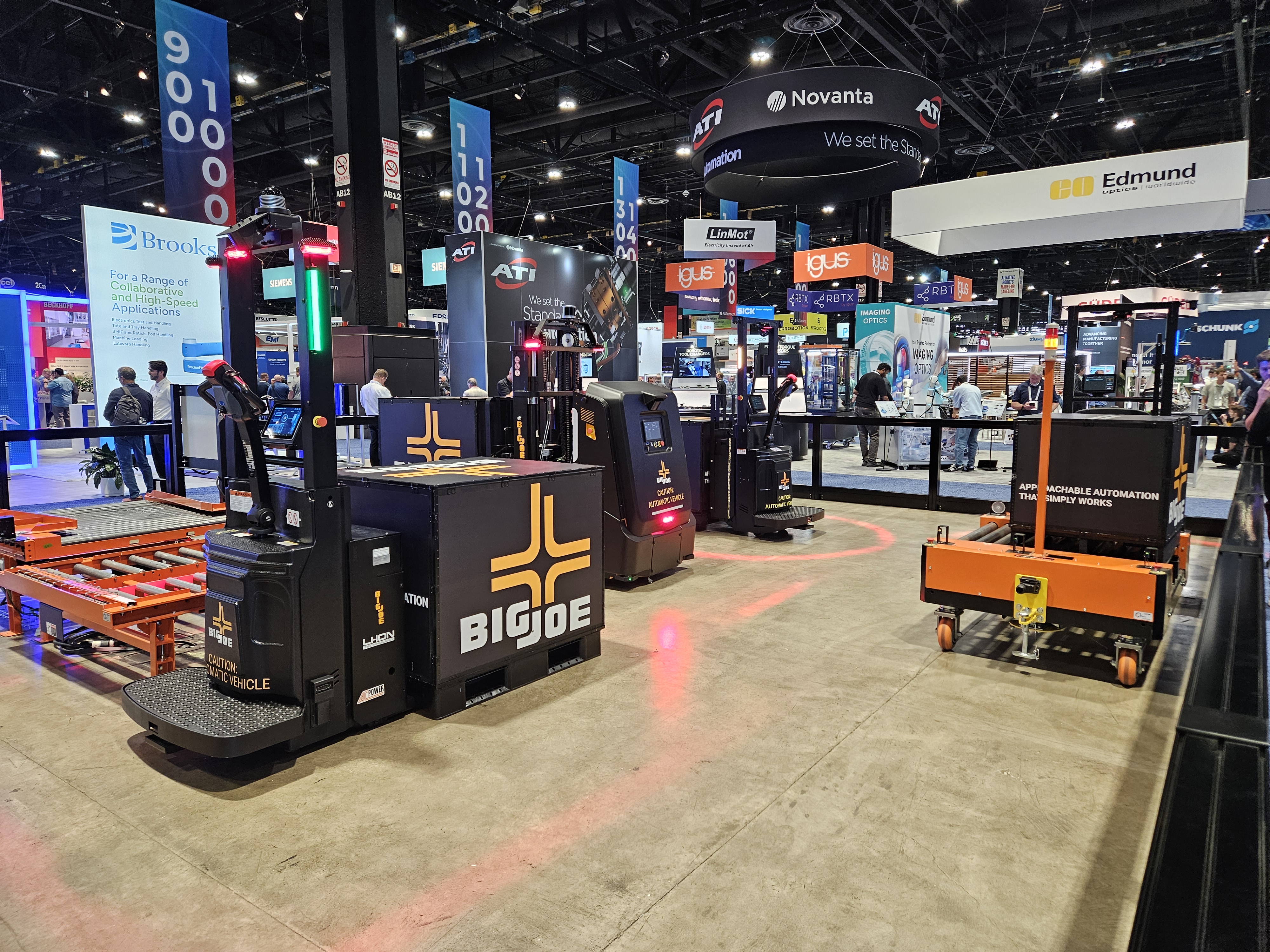 Trade show exhibition floor with multiple vendor booths, equipment displays, and overhead signage including Novanta and Edmund branding.