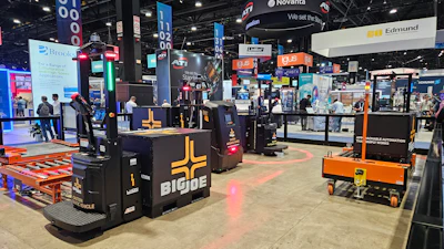 Trade show exhibition floor with multiple vendor booths, equipment displays, and overhead signage including Novanta and Edmund branding.
