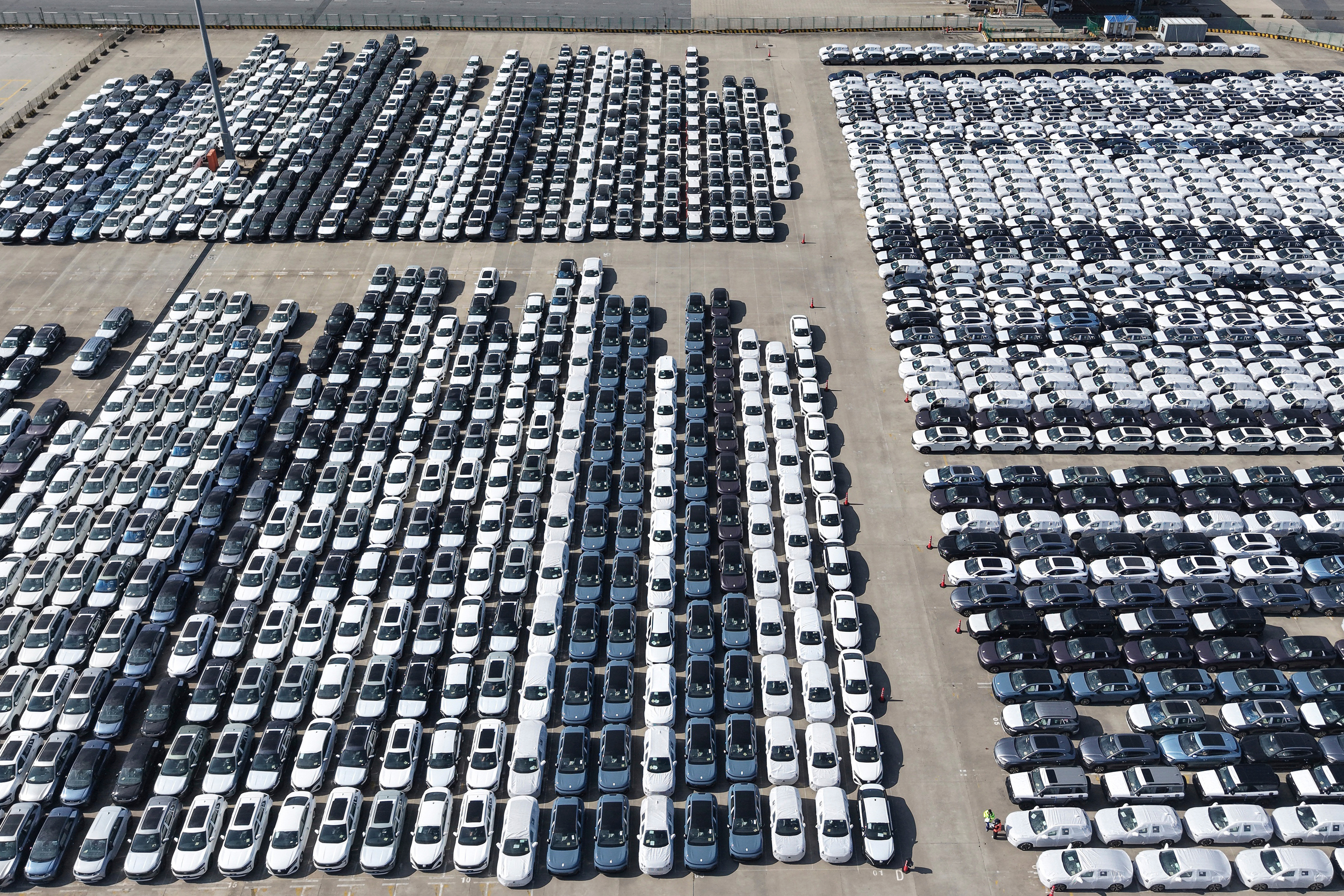 Aerial view of large vehicle storage lot with hundreds of cars arranged in organized rows on concrete surface