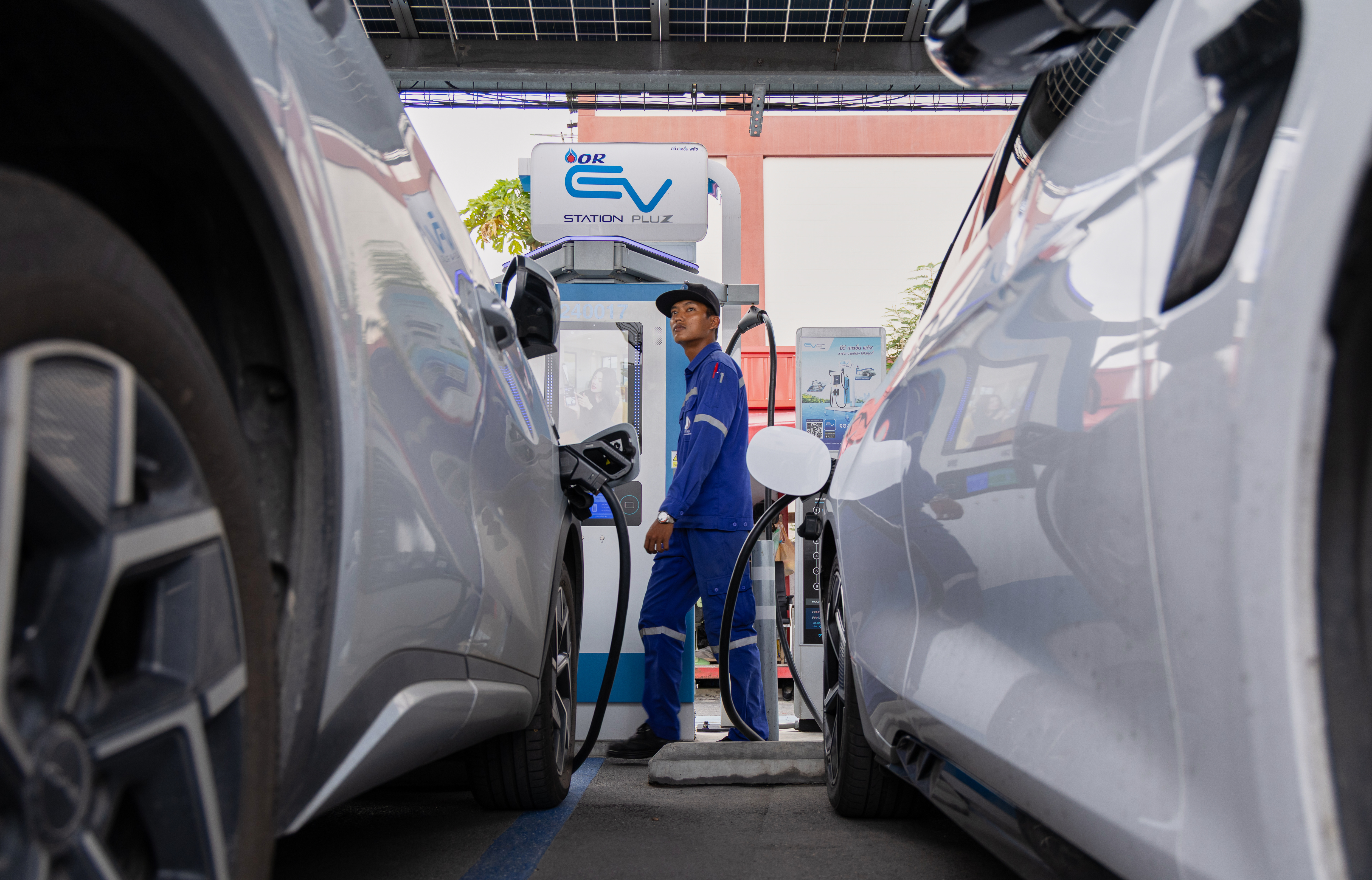 Technician operating electric vehicle charging station between parked cars at EV charging facility