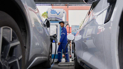 Technician operating electric vehicle charging station between parked cars at EV charging facility