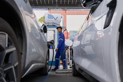 Technician operating electric vehicle charging station between parked cars at EV charging facility