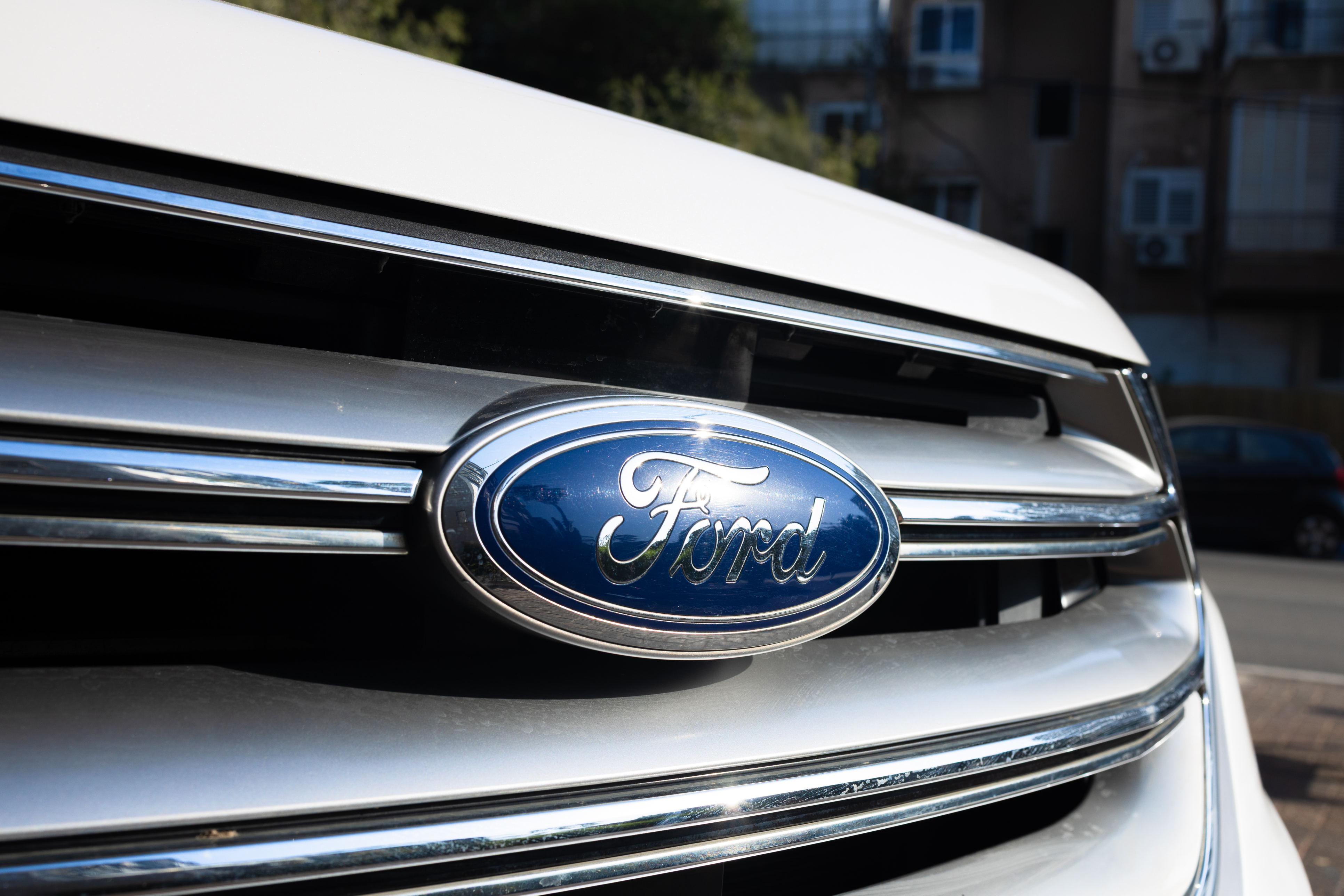 Ford logo emblem on vehicle grille with chrome trim and urban background