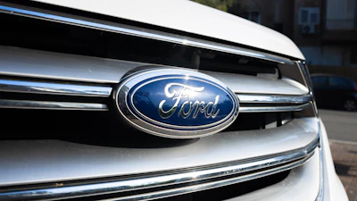 Ford logo emblem on vehicle grille with chrome trim and urban background