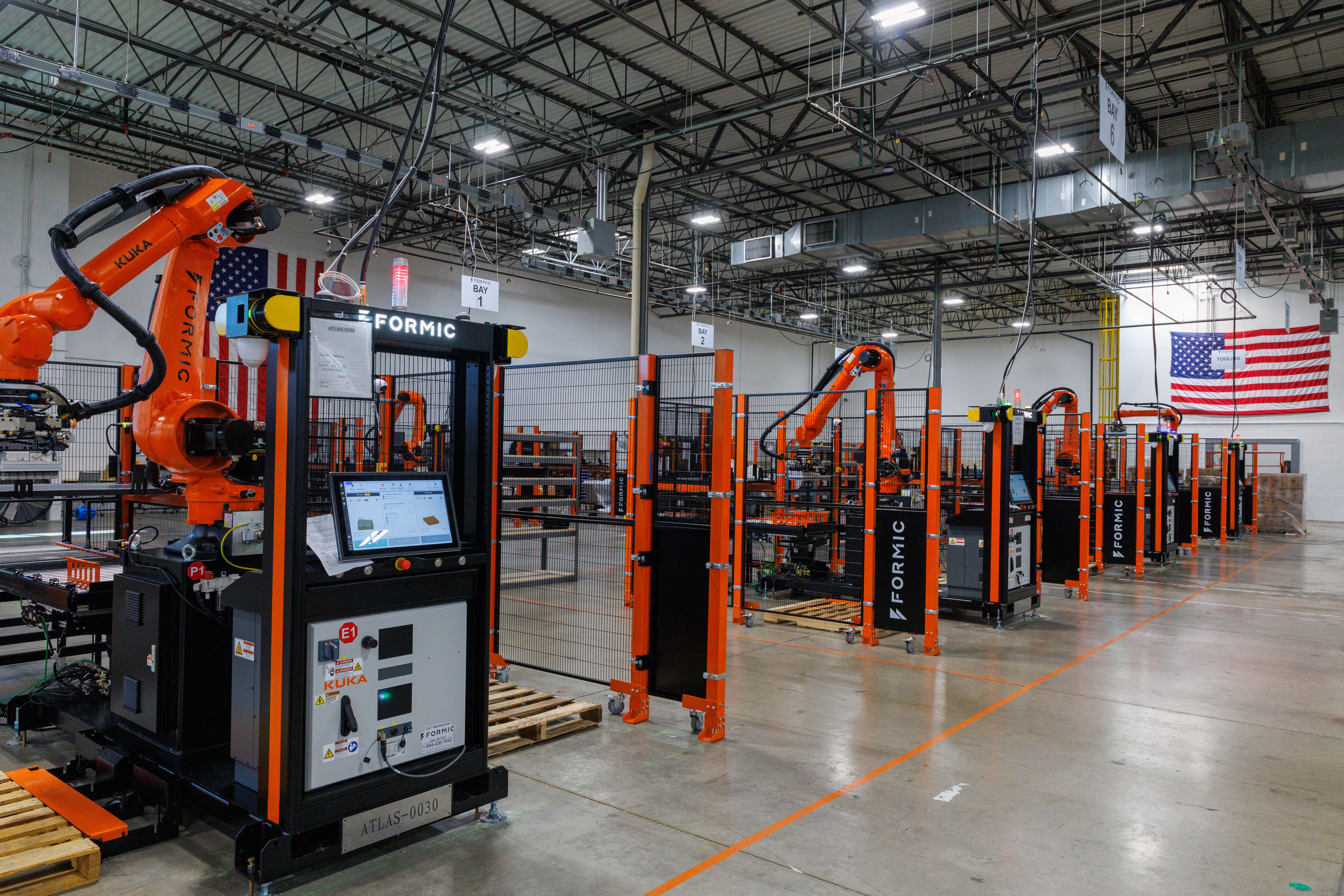 Industrial manufacturing facility with orange robotic welding equipment and machinery in a warehouse setting with American flag
